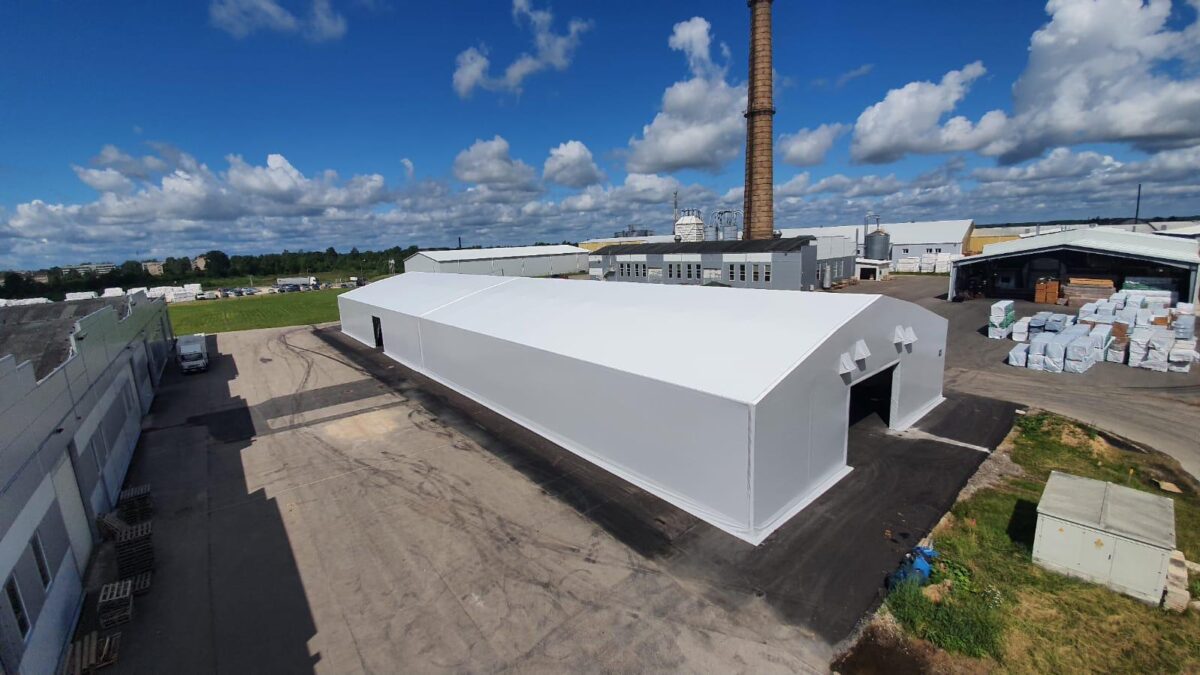 En hvit isolert talthall fra Hallgruppen er plassert på en industriplass under en blå himmel.