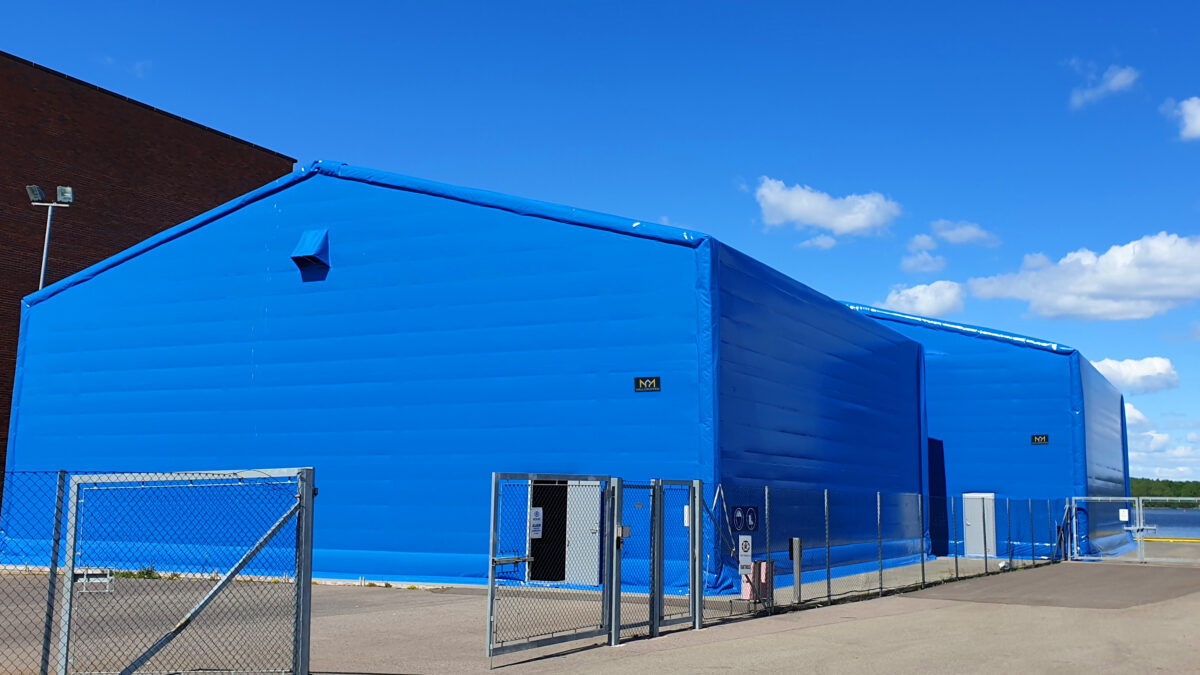 En stor blå isolert talthall fra Hallgruppen står på en asfaltert overflate under en klarblå himmel.