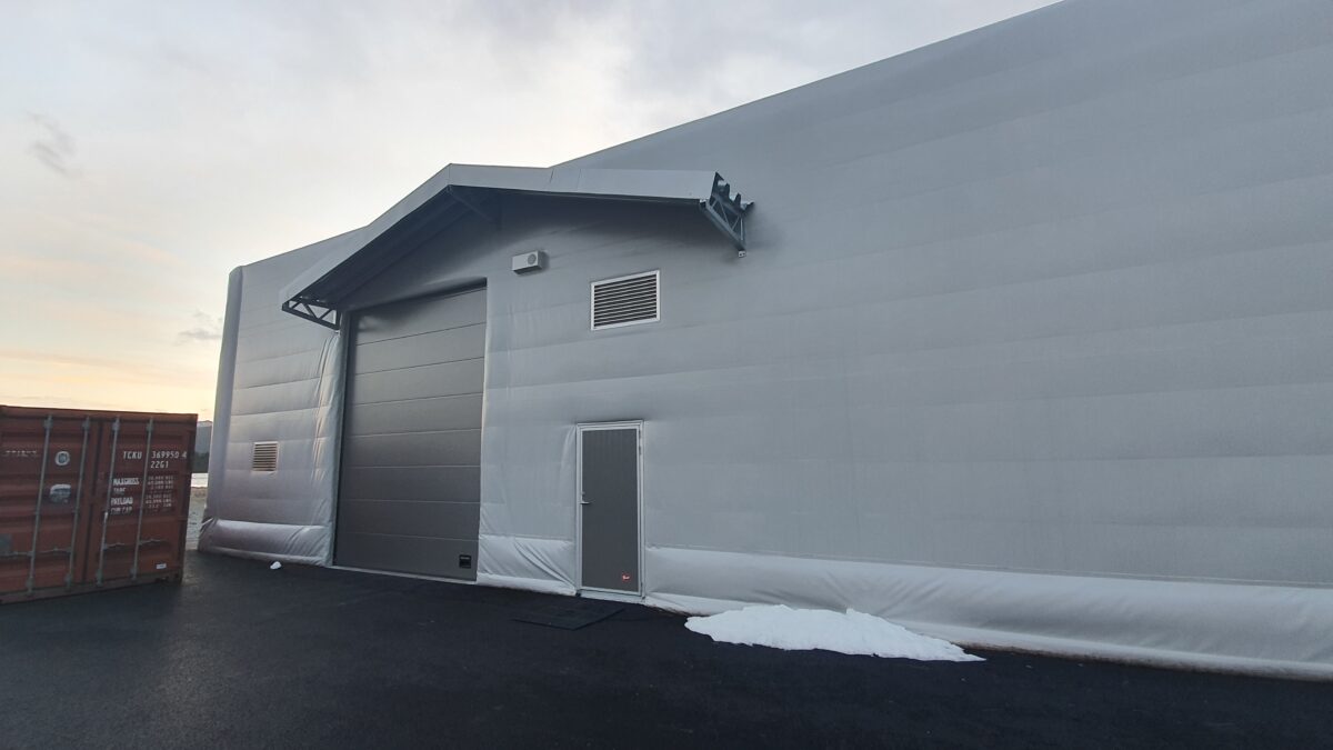 En isolert talthall fra Hallgruppen står på en asfaltert overflate med en rød container i nærheten.