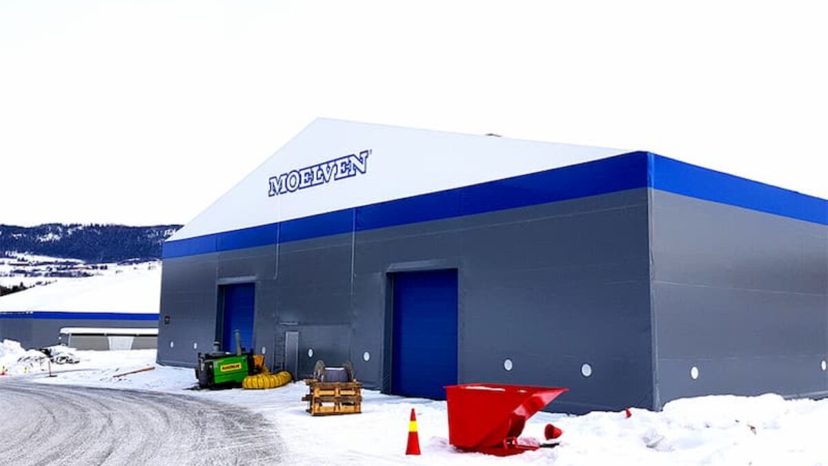 En isolert talthall med blå dører og logoen "Moelven", oppført av Hallgruppen, i et vintermiljø.